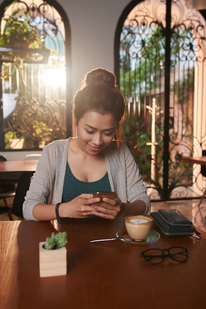 Foto gratuita mujer joven asiática enviando mensajes de texto en café