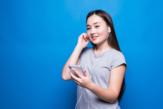 Mujer joven asiática escuchando audiolibros a través de auriculares en la pared azul