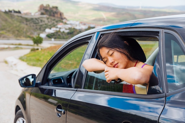 Mujer joven asiática que duerme mientras que se inclina en la ventana del coche