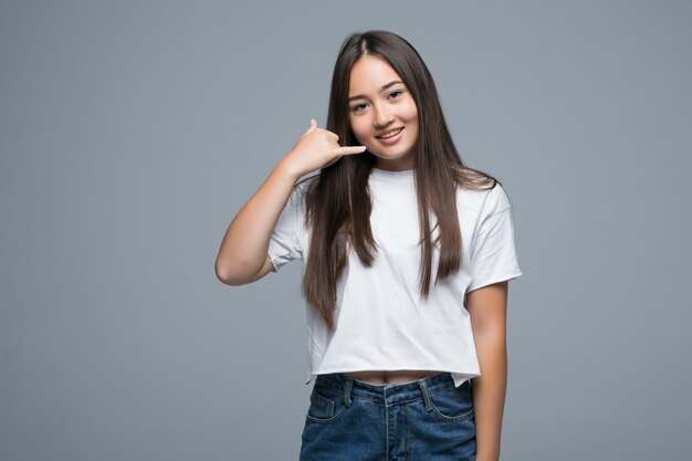 Mujer joven asiática sobre fondo gris aislado haciendo gesto de teléfono. Llámame señal de vuelta