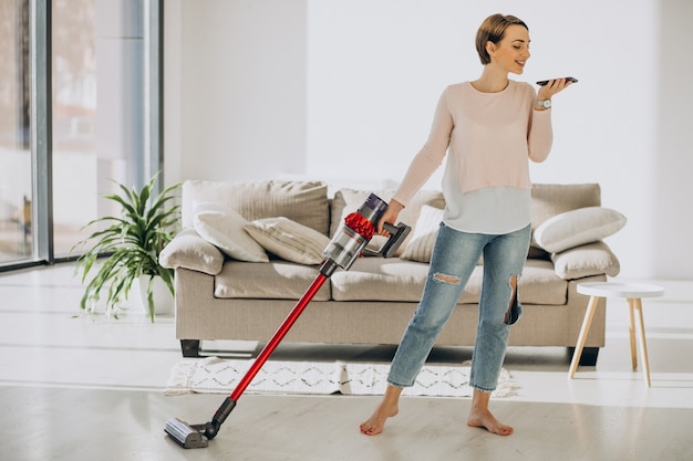Mujer joven con aspiradora recargable limpiando en casa