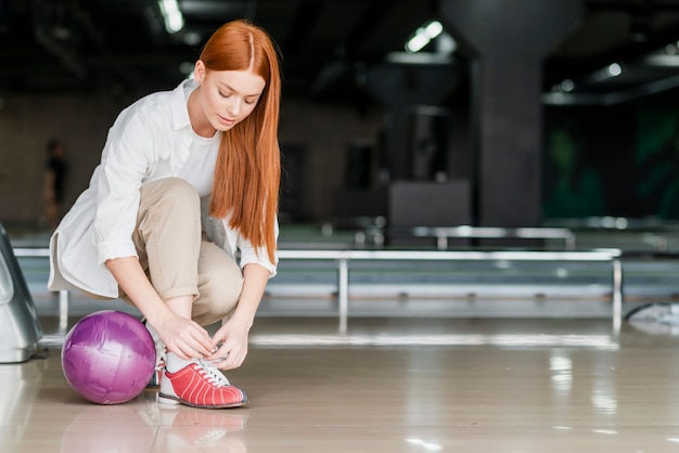 Mujer joven atar cordones de los zapatos en un club de bolos