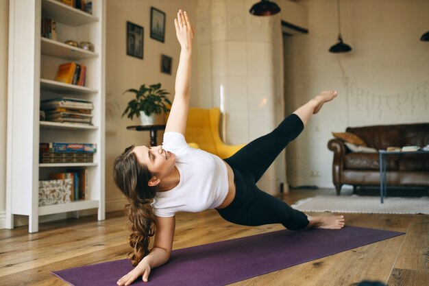 Mujer joven atlética enérgica haciendo ejercicio en el interior, haciendo una pose de plancha lateral que ayuda a desarrollar fuerza en el núcleo, los brazos y las piernas.