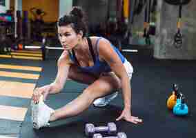 Foto gratuita una mujer joven atlética que estira su pierna en gimnasio