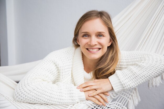 Mujer joven atractiva alegre en el suéter blanco que se relaja