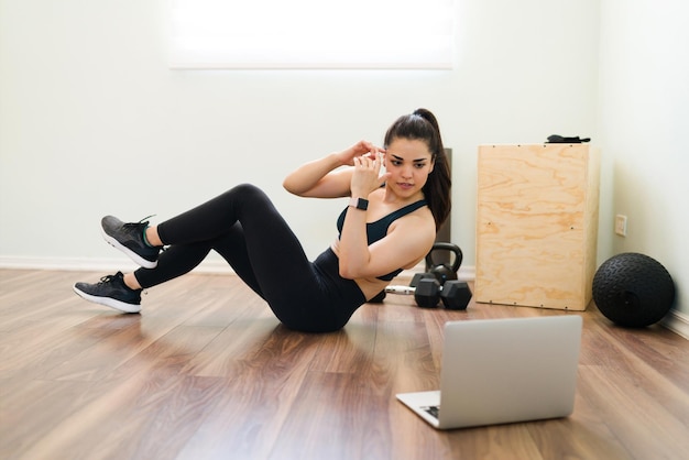 Mujer joven atractiva aprendiendo nuevos ejercicios con lecciones de fitness en línea. Una mujer en forma haciendo abdominales mientras ve un video tutorial en casa