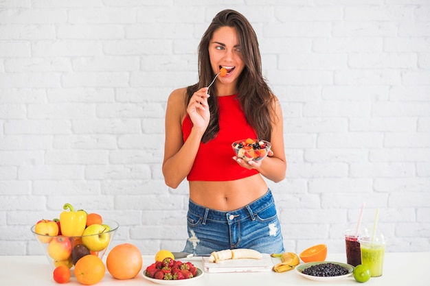 Foto gratuita mujer joven atractiva delgada comiendo ensalada de fruta fresca