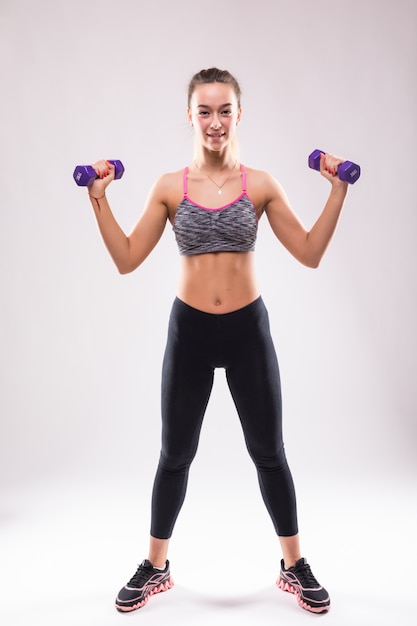 Mujer joven atractiva fitness chica hacer diferentes ejercicios aeróbicos con pesas en blanco vestidos con ropa deportiva