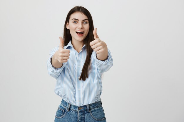 Mujer joven atractiva optimista mostrando el pulgar hacia arriba