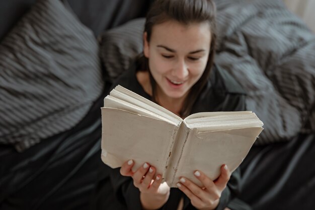 Mujer joven atractiva en pijama se relaja en la cama mientras lee un libro.