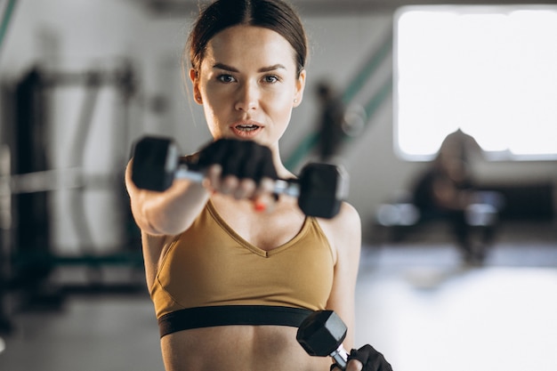 Mujer joven atractiva que ejercita con pesas en el gimnasio