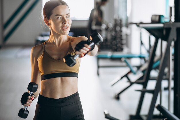 Mujer joven atractiva que ejercita con pesas en el gimnasio