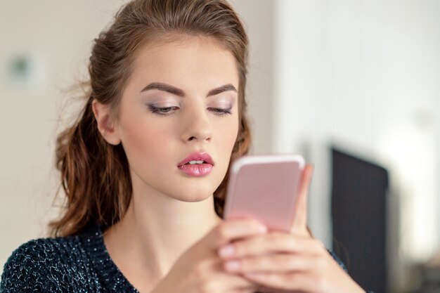 Mujer joven atractiva que mira su teléfono inteligente en casa. Mensaje de tipos de mujer en su teléfono inteligente.