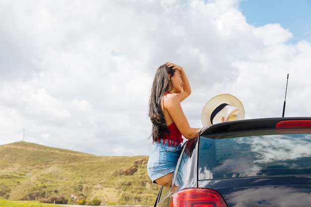 Mujer joven atractiva que se sienta en puerta de coche