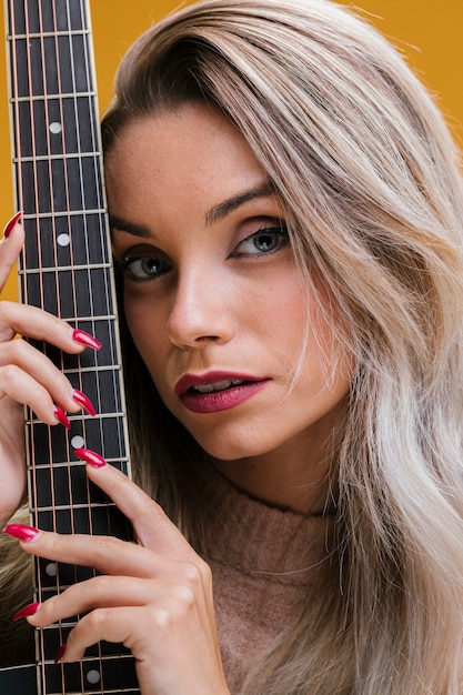 Mujer joven atractiva que sostiene la guitarra contra fondo amarillo