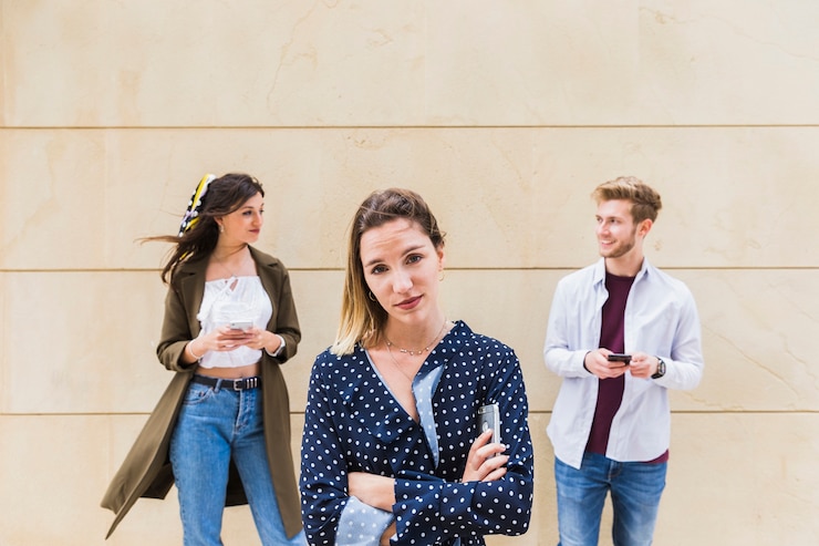 Foto gratuito una mujer joven atractiva que sostiene el teléfono móvil que se coloca delante de los amigos que miran uno a