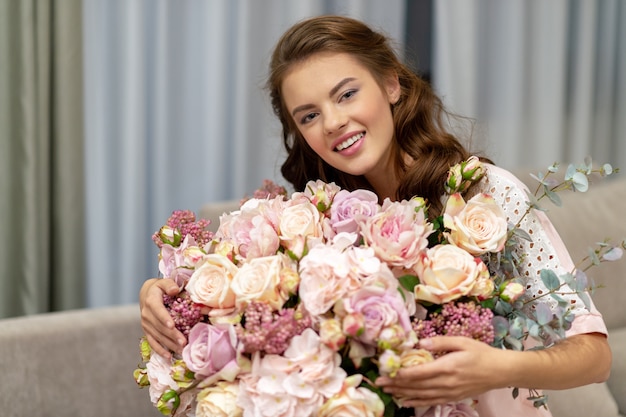 Mujer joven atractiva con ramo de cientos de flores pasa tiempo en casa.