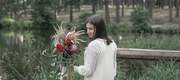 Mujer joven atractiva con un ramo de flores en el bosque junto al río