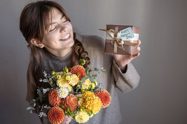 Mujer joven atractiva con un regalo del día de la madre y un ramo de flores de crisantemo en sus manos.