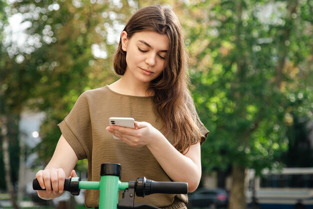 Mujer joven atractiva con un scooter eléctrico de alquiler en un día soleado