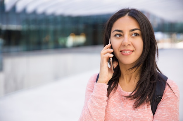 Mujer joven atractiva sonriente que comunica en el teléfono móvil