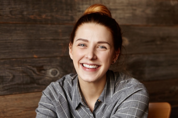 Foto gratuita mujer joven atractiva con una sonrisa encantadora que se siente feliz y libre después de graduarse de la universidad, relajarse en el café, esperar comida y hacer planes para el futuro. jengibre mujer descansando en el interior