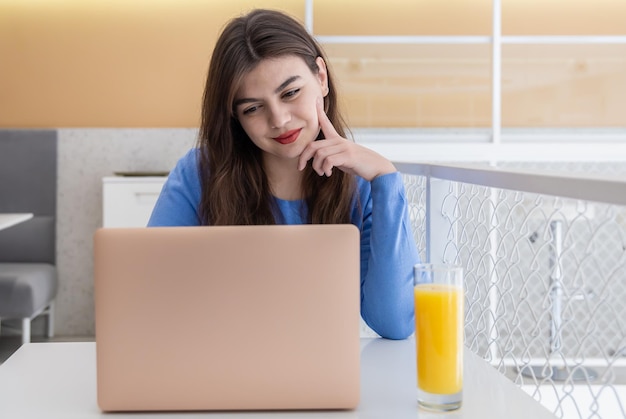 Mujer joven atractiva en un suéter azul trabaja en un portátil en un café