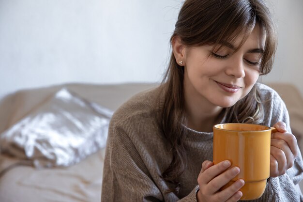 Mujer joven atractiva con una taza de bebida caliente sobre un fondo borroso