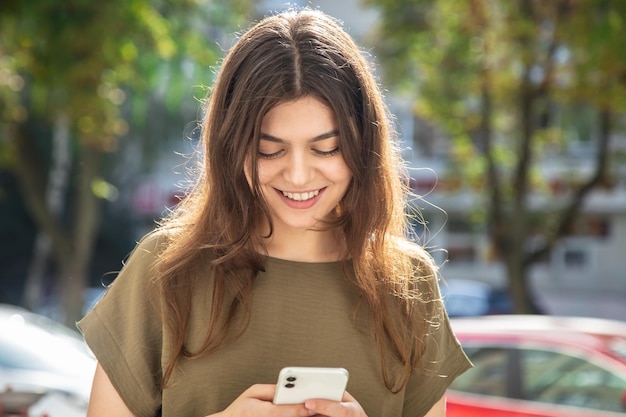 Mujer joven atractiva con un teléfono inteligente en el fondo de la calle