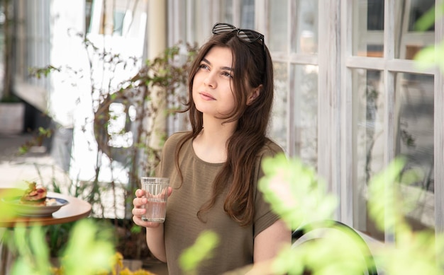 Mujer joven atractiva con un vaso de agua en un día de verano en la terraza de un café