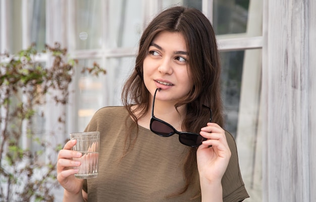 Mujer joven atractiva con un vaso de agua con gafas de sol