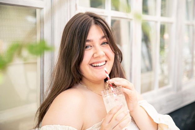 Mujer joven atractiva con un vaso de limonada en la terraza del café