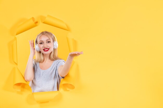 Mujer joven en auriculares apuntando a algo sobre fondo amarillo sonidos de audio ultrasonido