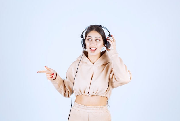 Mujer joven con auriculares apuntando o notando a alguien de la izquierda