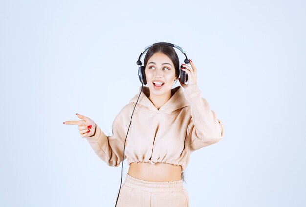 Mujer joven con auriculares apuntando o notando a alguien de la izquierda