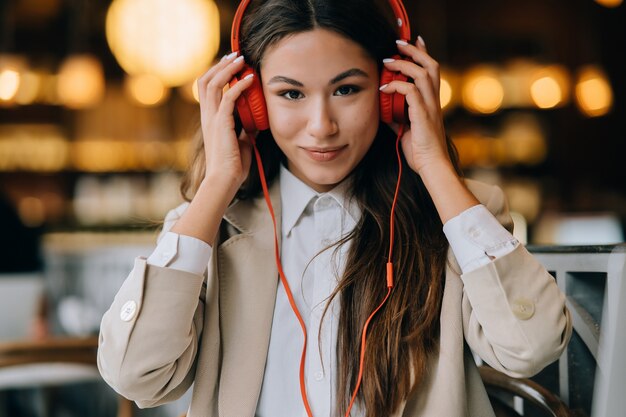 Mujer joven con auriculares escucha música mientras está sentado en cafés
