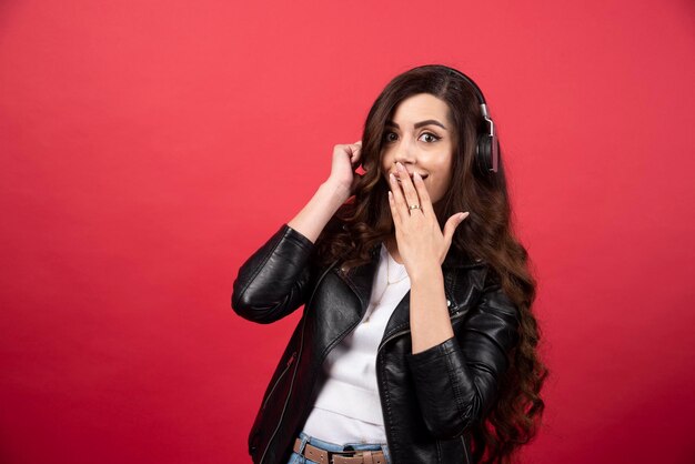 Mujer joven con auriculares y posando sobre un fondo rojo. Foto de alta calidad