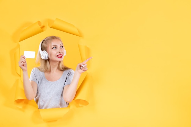 Mujer joven en auriculares con tarjeta de crédito en música de ultrasonido de fondo amarillo
