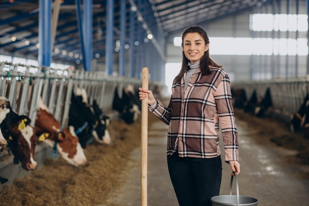 Mujer joven con balde y en el establo alimentando vacas