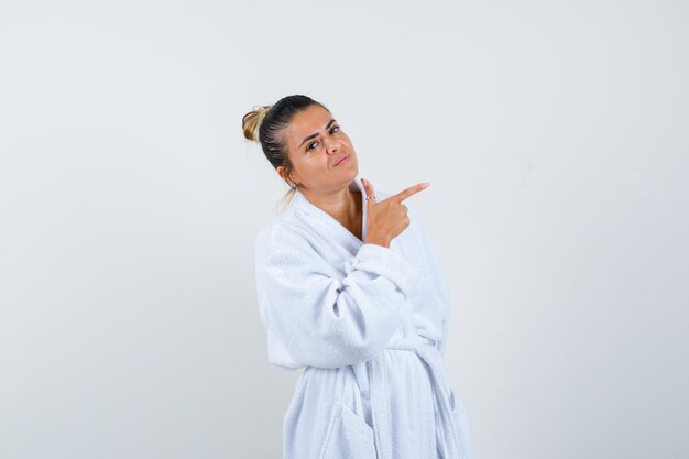 Mujer joven en bata de baño apuntando a un lado y mirando confiado