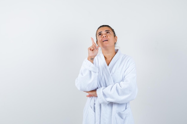 Mujer joven en bata de baño apuntando a un lado y mirando confiado