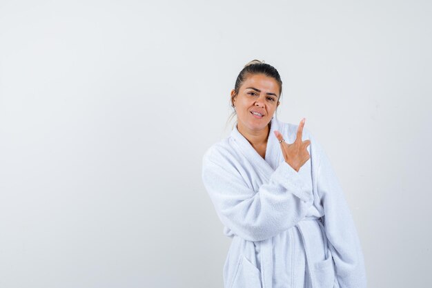 Mujer joven en bata de baño apuntando a un lado y mirando confiado