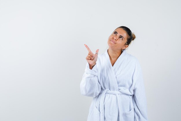 Mujer joven en bata de baño apuntando a un lado y mirando confiado