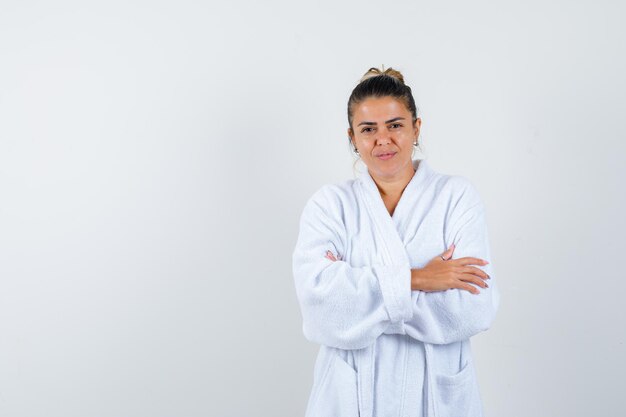 Mujer joven en bata de baño blanca de pie con los brazos cruzados y mirando feliz