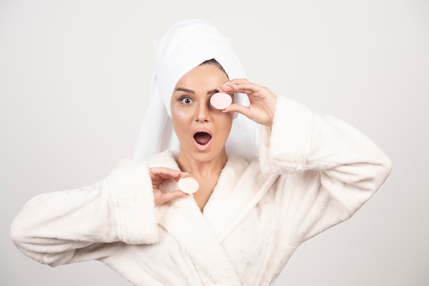 Mujer joven en bata de baño haciendo maquillaje.