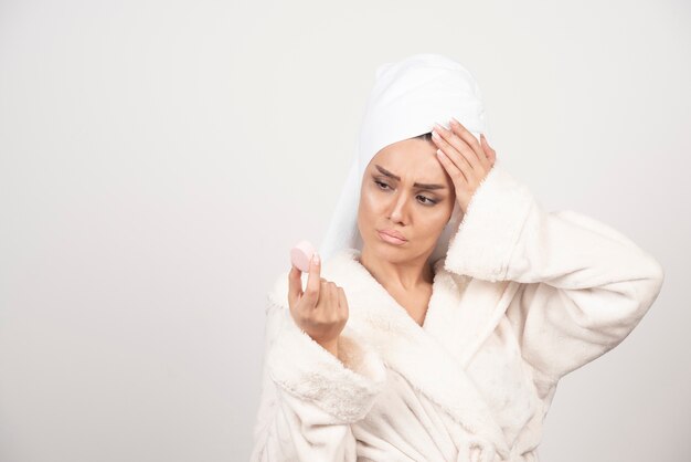 Mujer joven en bata de baño haciendo maquillaje.