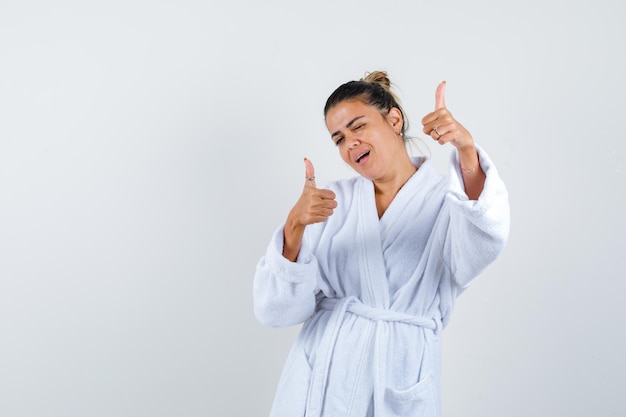 Foto gratuita mujer joven en bata de baño mostrando los pulgares hacia arriba y mirando confiado