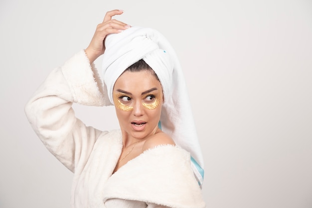 Mujer joven en bata de baño y parches cosméticos en los ojos posando