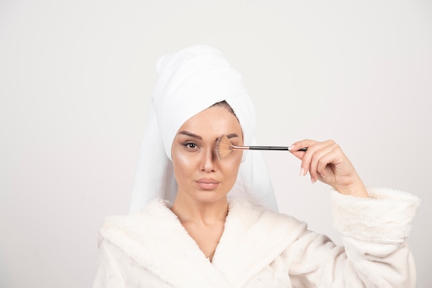 Mujer joven en una bata de baño con pincel de maquillaje.