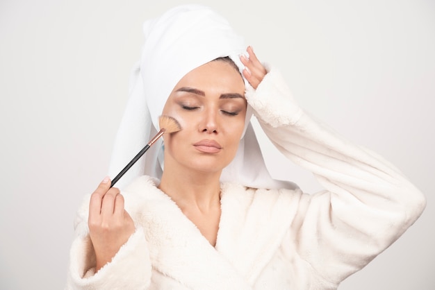 Mujer joven en una bata de baño con pincel de maquillaje.